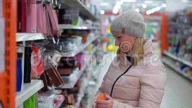 一位戴着帽子和<strong>羽绒服</strong>的中年妇女在超市里选择了一个红色的热水瓶。